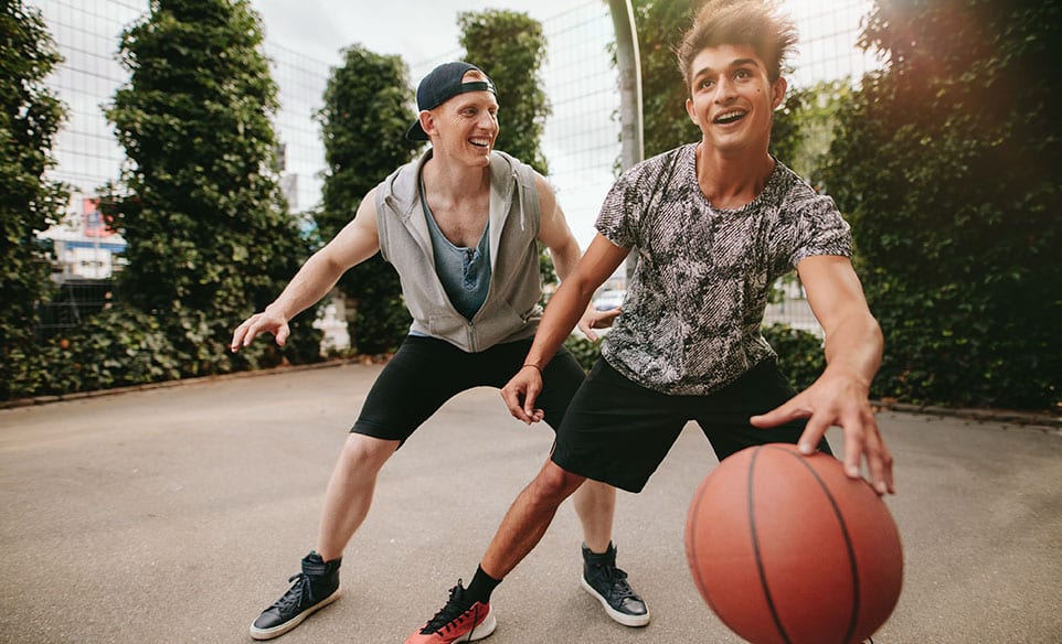 Two teens smiling playing basketball