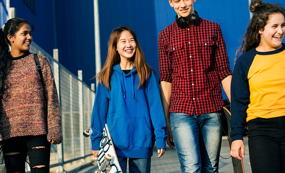 Group of teens walking with skateboards and smiling